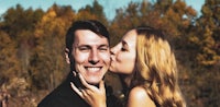 a man and woman kissing in front of trees