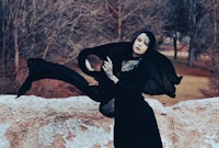 a woman in a black dress is posing in the woods