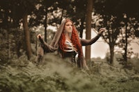 a woman with red hair standing in the woods
