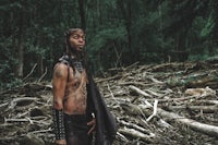 a man with tattoos standing in the woods