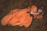 a girl in an orange dress laying in a field